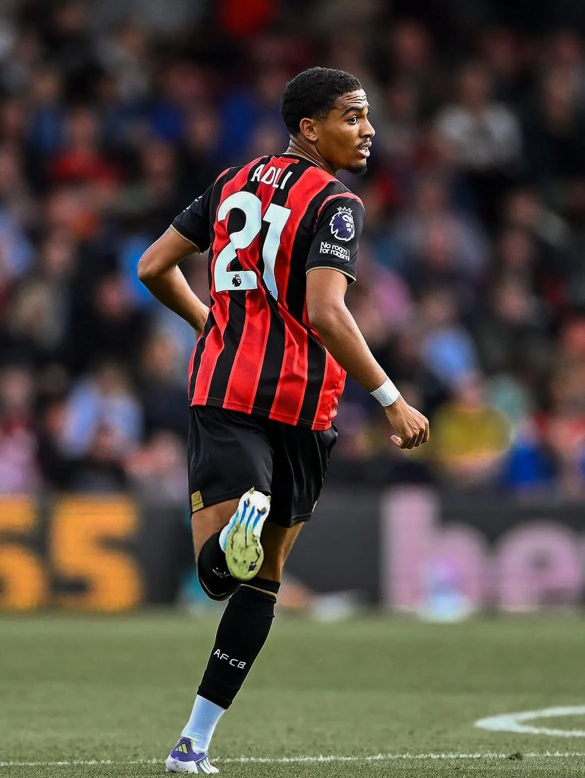 Amine Adli turning on the pitch in a red and black striped shirt.