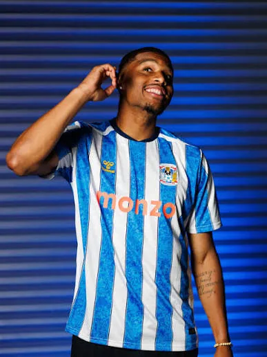 Aurèle Amenda laughing in a sky-blue and white striped shirt, a hand at his ear.