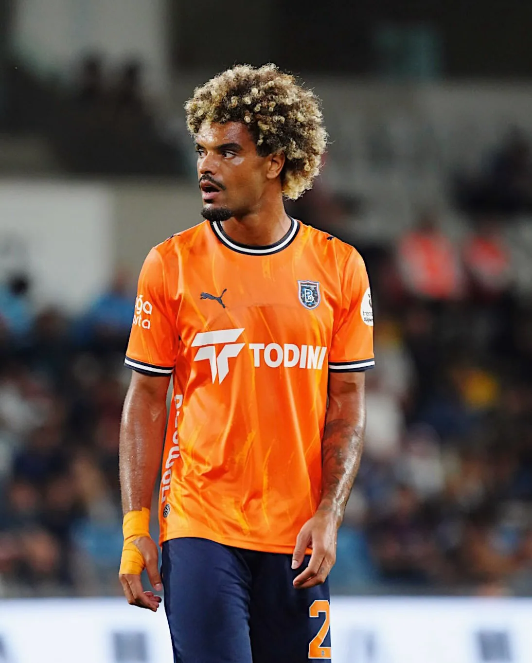 Christopher Opéri on the pitch in an orange shirt, looking away from the camera.