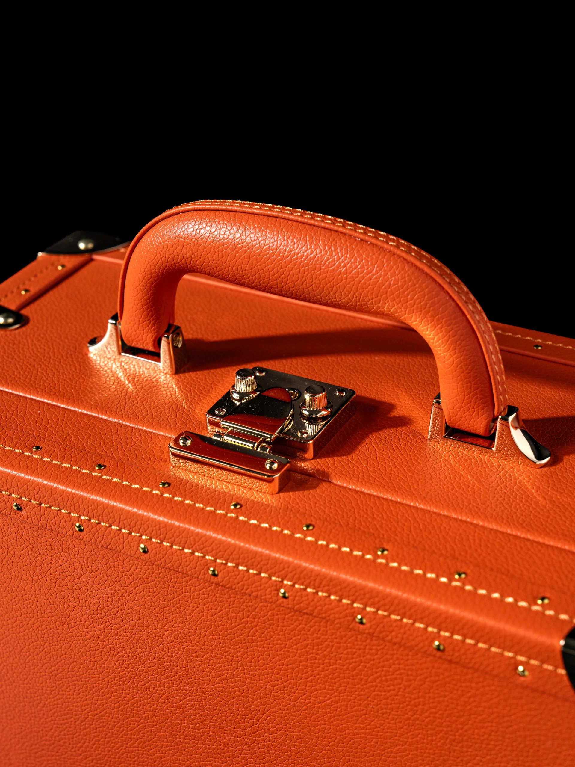 Macro of the trunk's orange leather handle and its brass clasp.