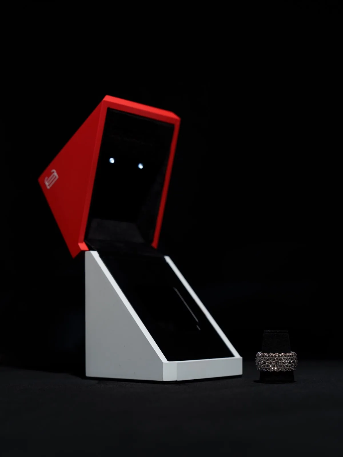 The écrin open, the red lid raised above a white wedge of a base.