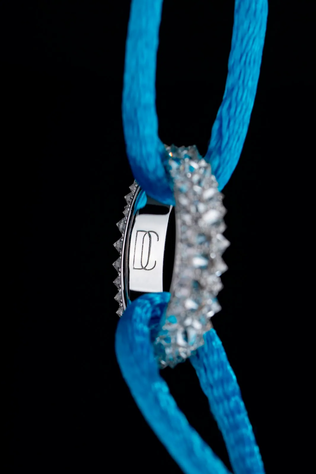 The ring seen in profile on the cord, its polished side engraved with the maison's monogram.
