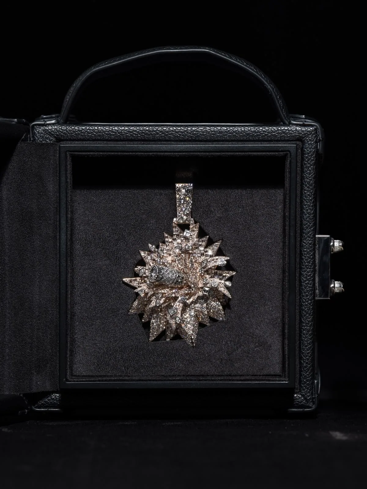 The écrin open, a diamond starburst pendant held in its dark suede panel.