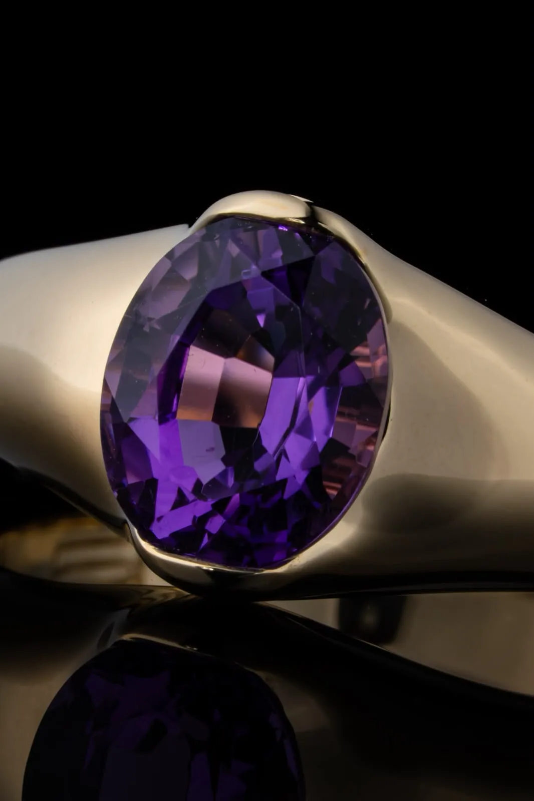 Macro of the violet stone, its facets held between two polished gold shoulders.
