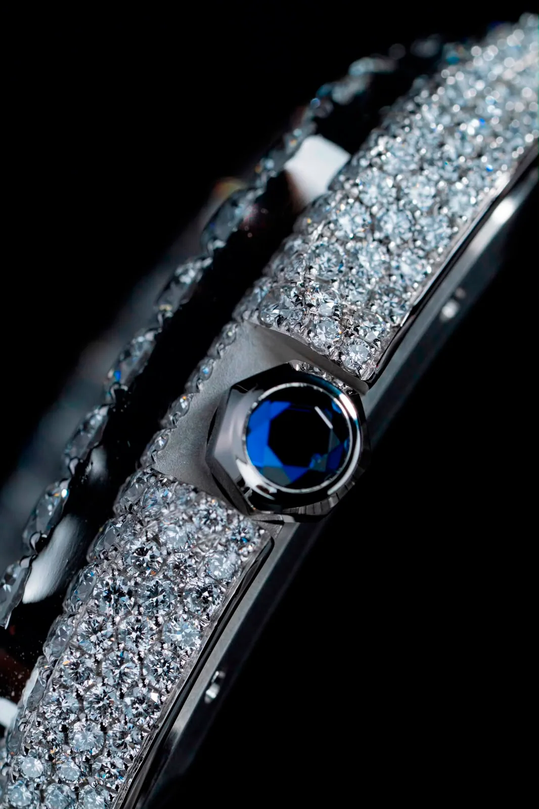 The crown and its blue cabochon, set between bands of pavé diamonds on the case flank.