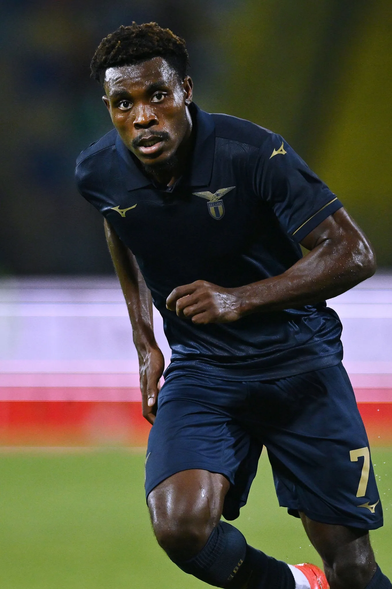 Fisayo Dele-Bashiru running on the pitch in a dark shirt, looking ahead.