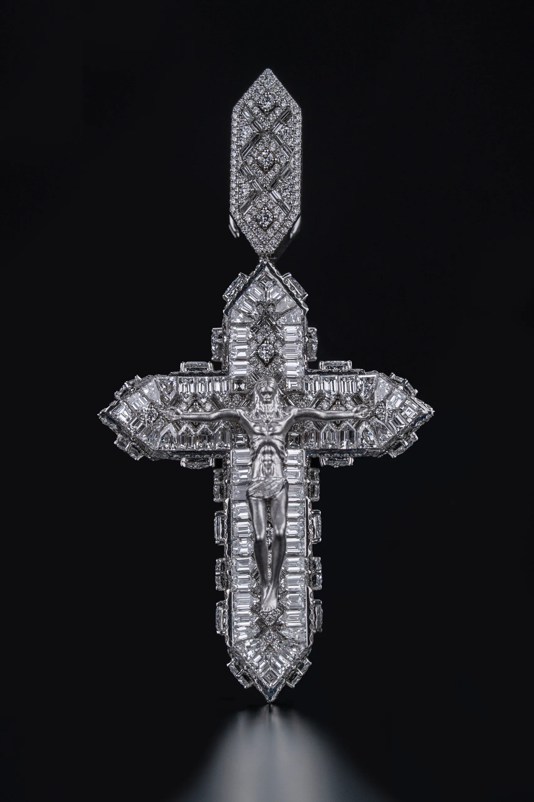 The cross pendant lit from a single source against near-black.