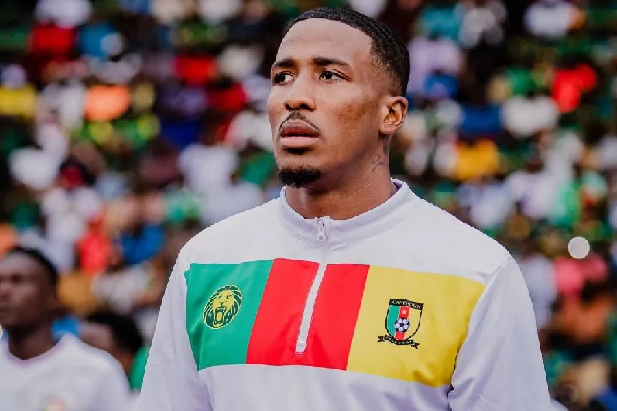 Jackson Tchatchoua in a white Cameroon jacket, looking into the distance.