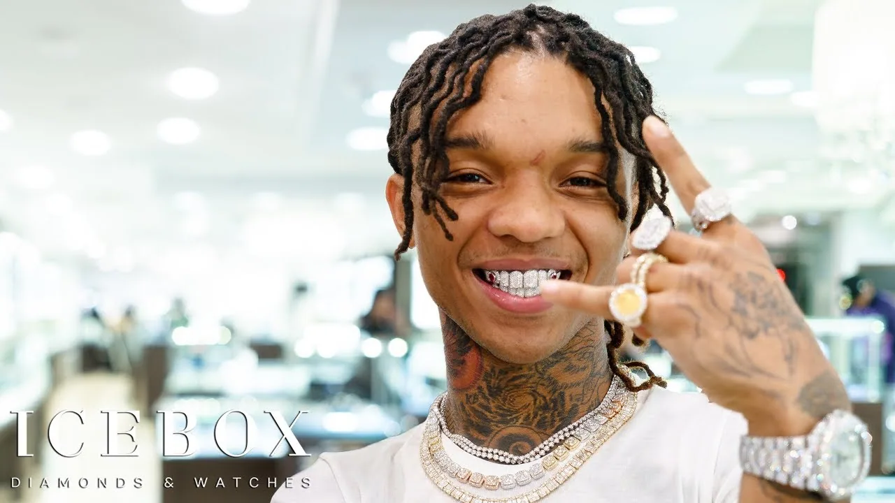 Swae Lee laughing into the camera, his locs falling around his face, a hand raised beside it.