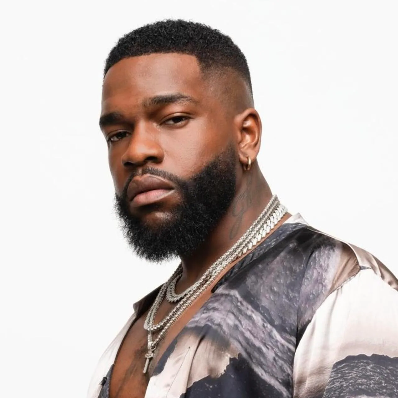Tayc in a close studio portrait, looking into the camera over his shoulder, chains at his neck.